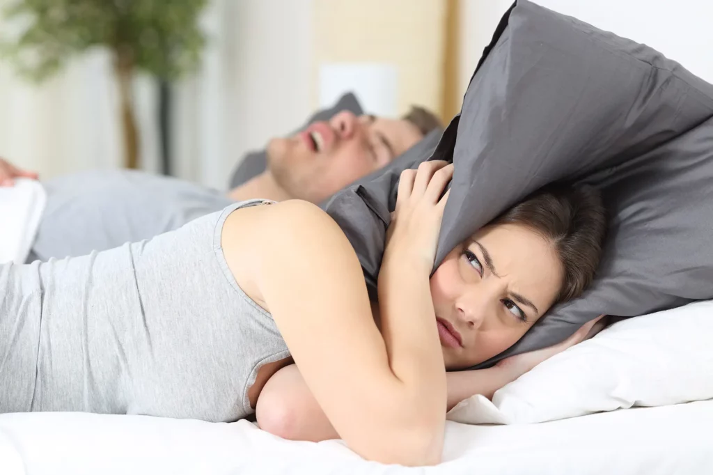 Ein Mann schnarcht, und seine Frau hält sich die Ohren zu